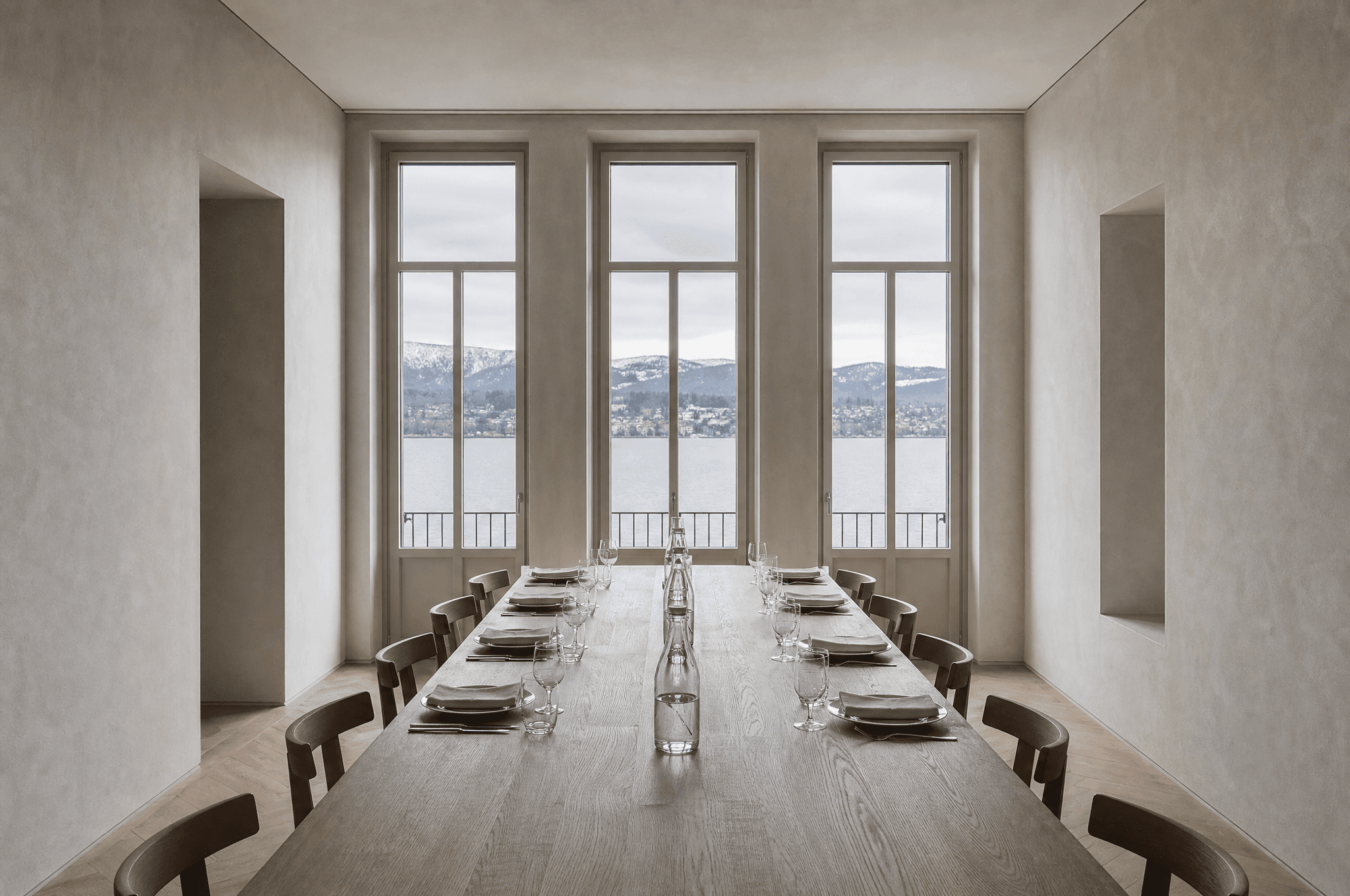 A long oak table laid for sixteen in a Zurich townhouse, tall windows onto the lake in winter light.